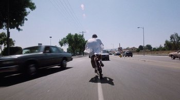 Movie still from “Innerspace” (1987), directed by Joe Dante – A man riding a bike down the middle of the street; Wide shot, Low angle