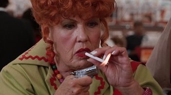 Movie still from “Innerspace” (1987), directed by Joe Dante – An older woman lighting a cigarette with a lighter in her mouth; Close Up shot, Low angle