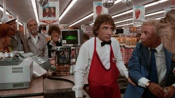 Movie still from “Innerspace” (1987), directed by Joe Dante – A man wearing a red apron in a store; Medium shot, Over the shoulder angle