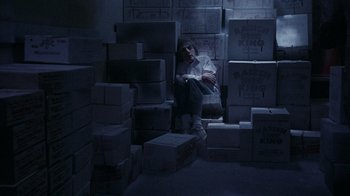 Movie still from “Innerspace” (1987), directed by Joe Dante – A man sitting on a pile of boxes in a dark room; Wide shot, High angle