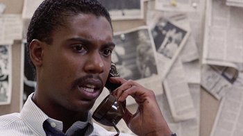 Movie still from “Innerspace” (1987), directed by Joe Dante – A man talking on a phone in front of newspapers; Close Up shot, Low angle