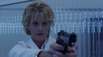 Movie still from “Innerspace” (1987), directed by Joe Dante – A woman is holding a gun in her hand; Close Up shot, Low angle