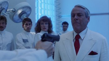 Movie still from “Innerspace” (1987), directed by Joe Dante – A group of people standing around a man holding a gun; Medium shot, Over the shoulder angle