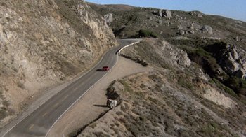 Movie still from “Innerspace” (1987), directed by Joe Dante – A red car driving down the side of a mountain road; Extreme Wide shot, High angle