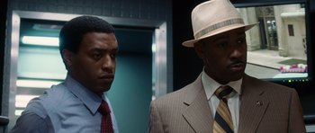 Movie still from “Inside Man” (2006), directed by Spike Lee – A man in a suit and a hat standing next to another man in a suit; Close Up shot, Low angle