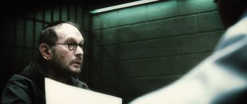 Movie still from “Inside Man” (2006), directed by Spike Lee – A man with glasses sitting in a room; Close Up shot, Over the shoulder angle