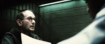 Movie still from “Inside Man” (2006), directed by Spike Lee – A man sitting in front of a brick wall in a room; Close Up shot, Over the shoulder angle