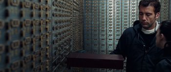 Movie still from “Inside Man” (2006), directed by Spike Lee – A person sitting at a table in front of a wall of card catalogs; Medium shot, Low angle