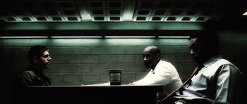 Movie still from “Inside Man” (2006), directed by Spike Lee – A man sitting at a table looking at a cell phone; Wide shot, Over the shoulder angle