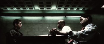 Movie still from “Inside Man” (2006), directed by Spike Lee – A man sitting at a table with a cell phone in front of him; Medium shot, Over the shoulder angle