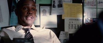 Movie still from “Inside Man” (2006), directed by Spike Lee – A man wearing a white dress shirt and a black tie in front of a bunch of posters; Close Up shot, Low angle
