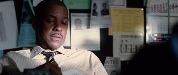 Movie still from “Inside Man” (2006), directed by Spike Lee – A man sitting in front of a bunch of missing posters; Close Up shot, Low angle