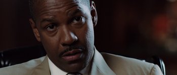 Movie still from “Inside Man” (2006), directed by Spike Lee – A person wearing a suit and tie; Close Up shot, Over the shoulder angle