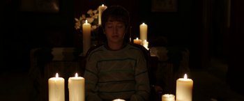 Movie still from “Insidious: Chapter 2” (2013), directed by James Wan – A young boy sitting in a chair in front of candles; Medium shot, High angle