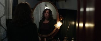 Movie still from “Insidious: Chapter 2” (2013), directed by James Wan – A woman looking in the mirror in front of a lamp; Medium shot, Over the shoulder angle