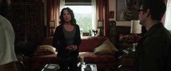 Movie still from “Insidious: Chapter 2” (2013), directed by James Wan – A woman standing in front of a couch in a living room; Medium shot, Over the shoulder angle