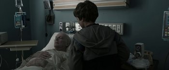Movie still from “Insidious: Chapter 2” (2013), directed by James Wan – A young boy standing next to an older man in a hospital bed; Medium shot, Over the shoulder angle
