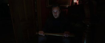 Movie still from “Insidious: Chapter 2” (2013), directed by James Wan – A man holding a baseball bat in a dark room; Medium shot, High angle