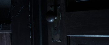 Movie still from “Insidious: Chapter 2” (2013), directed by James Wan – A door knob on a wooden door with a dark background; Extreme Close Up shot, Overhead angle
