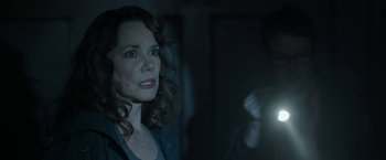 Movie still from “Insidious: Chapter 2” (2013), directed by James Wan – A woman is looking at the camera in a dark room; Close Up shot, Over the shoulder angle