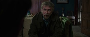 Movie still from “Insidious: Chapter 2” (2013), directed by James Wan – An older man sitting on a couch in a living room; Medium shot, Over the shoulder angle