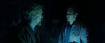 Movie still from “Insidious: Chapter 2” (2013), directed by James Wan – Two men are talking in a dimly - lit room; Medium shot, Over the shoulder angle