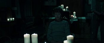 Movie still from “Insidious: Chapter 2” (2013), directed by James Wan – A boy sitting in a chair in front of some candles; Medium shot, High angle