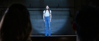 Movie still from “Insidious: Chapter 3” (2015), directed by Leigh Whannell – A woman standing on a stage wearing jeans and a white shirt; Wide shot, Low angle