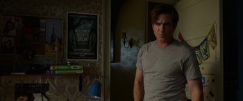 Movie still from “Insidious: Chapter 3” (2015), directed by Leigh Whannell – A man standing in front of a wall with a poster on the wall; Medium shot, Over the shoulder angle