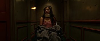 Movie still from “Insidious: Chapter 3” (2015), directed by Leigh Whannell – A woman with a neck brace sitting in a chair; Medium shot, Low angle