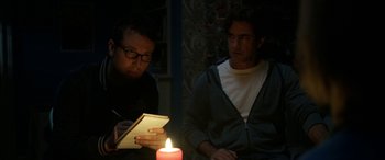 Movie still from “Insidious: Chapter 3” (2015), directed by Leigh Whannell – Two men sitting in a dimly - lit room with a lit candle; Medium shot, Over the shoulder angle