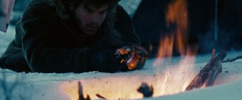 Movie still from “Into the Wild” (2007), directed by Sean Penn – A man is laying on the ground near a fire; Close Up shot, Over the shoulder angle