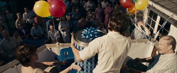 Movie still from “Into the Wild” (2007), directed by Sean Penn – A man standing in front of a crowd holding a blue bow; Medium shot, Over the shoulder angle