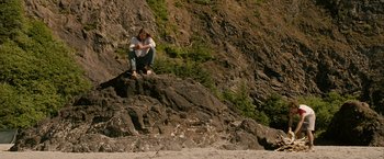 Movie still from “Into the Wild” (2007), directed by Sean Penn – A man sitting on top of a rock on the beach; Wide shot, High angle