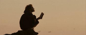 Movie still from “Into the Wild” (2007), directed by Sean Penn – A man reading a book while standing on a hill; Medium shot, Low angle