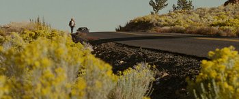 Movie still from “Into the Wild” (2007), directed by Sean Penn – A person walking down a road near a car; Extreme Wide shot, Low angle