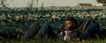 Movie still from “Into the Wild” (2007), directed by Sean Penn – A man laying in the grass eating something; Medium shot, Low angle