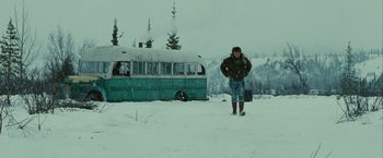 Movie still from “Into the Wild” (2007), directed by Sean Penn – A man standing in the snow next to an old bus; Wide shot, Low angle