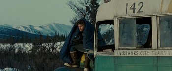 Movie still from “Into the Wild” (2007), directed by Sean Penn – A man sitting on the side of a bus with a sleeping bag on; Wide shot, Low angle