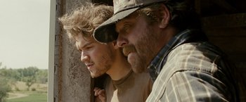 Movie still from “Into the Wild” (2007), directed by Sean Penn – Two men standing next to each other in front of a stone wall; Close Up shot, Over the shoulder angle