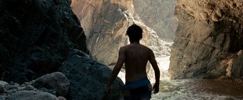 Movie still from “Into the Wild” (2007), directed by Sean Penn – A man standing in the water next to a rocky cliff; Wide shot, Low angle