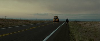 Movie still from “Into the Wild” (2007), directed by Sean Penn – A man riding a bike down the side of a road; Extreme Wide shot, Over the shoulder angle