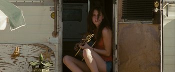 Movie still from “Into the Wild” (2007), directed by Sean Penn – A woman sitting on the side of a building playing a guitar; Wide shot, Low angle