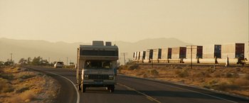 Movie still from “Into the Wild” (2007), directed by Sean Penn – An rv driving down a highway with a train in the background; Extreme Wide shot, Low angle