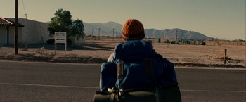 Movie still from “Into the Wild” (2007), directed by Sean Penn – A person riding a bike with a backpack; Wide shot, Over the shoulder angle