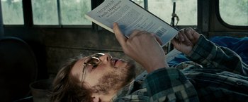 Movie still from “Into the Wild” (2007), directed by Sean Penn – A man reading a book while lying on the ground; Close Up shot, Over the shoulder angle
