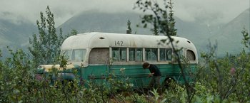 Movie still from “Into the Wild” (2007), directed by Sean Penn – A man working on the side of an old school bus; Wide shot, High angle