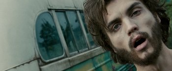Movie still from “Into the Wild” (2007), directed by Sean Penn – A person's face with a bus in the background; Close Up shot, Low angle