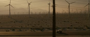 Movie still from “Into the Wild” (2007), directed by Sean Penn – A car driving down a road near a field of wind turbines; Extreme Wide shot, High angle