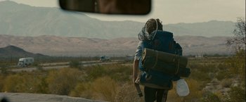 Movie still from “Into the Wild” (2007), directed by Sean Penn – A man with a backpack walking on the side of a road; Wide shot, Over the shoulder angle